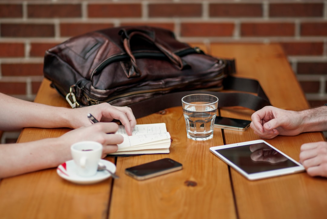 Two people having a meeting while displaying their iphone, ipad, and smartphone on the table.