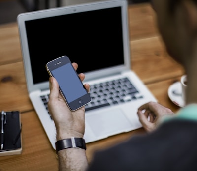 person holding black iPhone 4 front of MacBook Air
