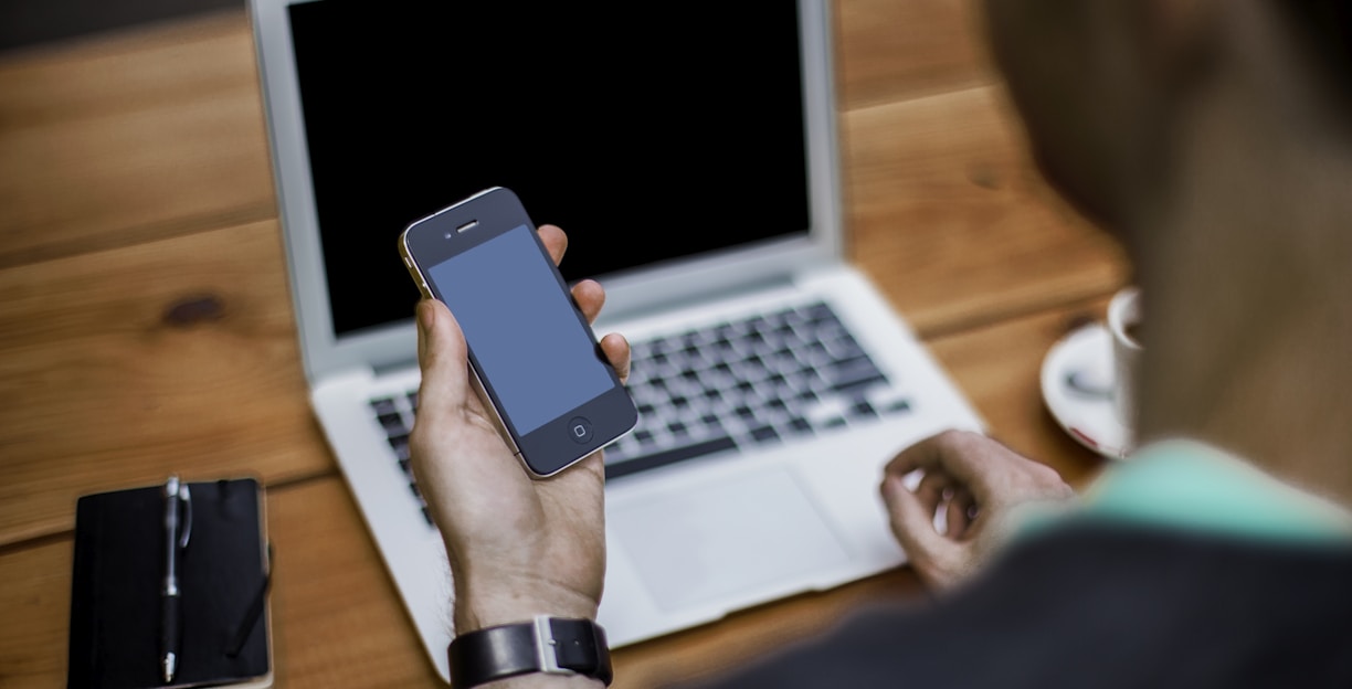 person holding black iPhone 4 front of MacBook Air