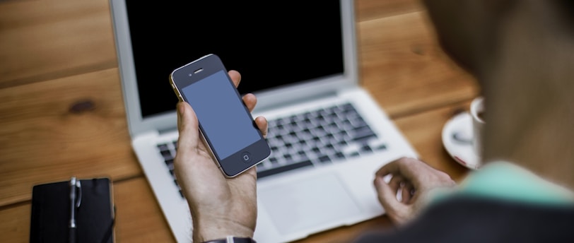 person holding black iPhone 4 front of MacBook Air