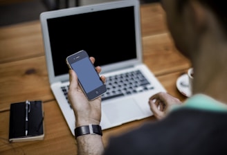 person holding black iPhone 4 front of MacBook Air