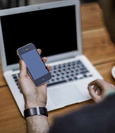 person holding black iPhone 4 front of MacBook Air