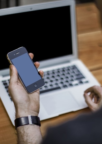 person holding black iPhone 4 front of MacBook Air