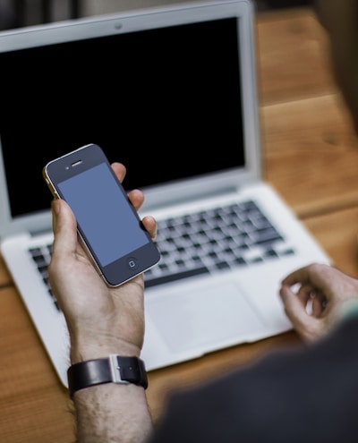 person holding black iPhone 4 front of MacBook Air
