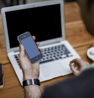 person holding black iPhone 4 front of MacBook Air