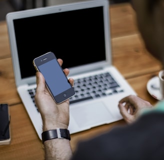 person holding black iPhone 4 front of MacBook Air
