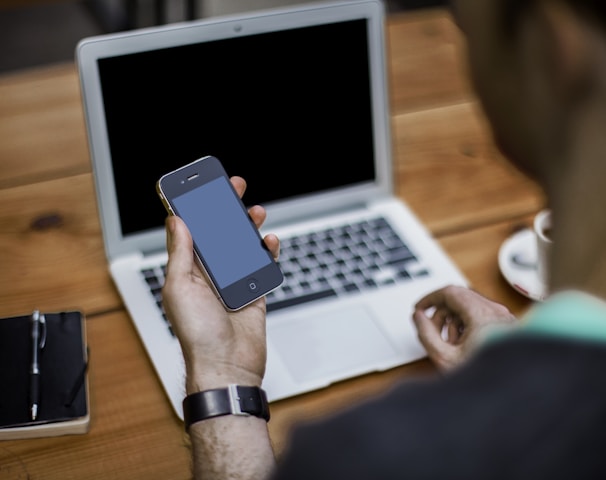 person holding black iPhone 4 front of MacBook Air