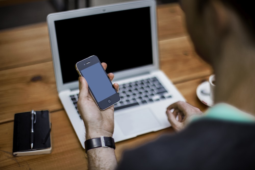 person holding black iPhone 4 front of MacBook Air