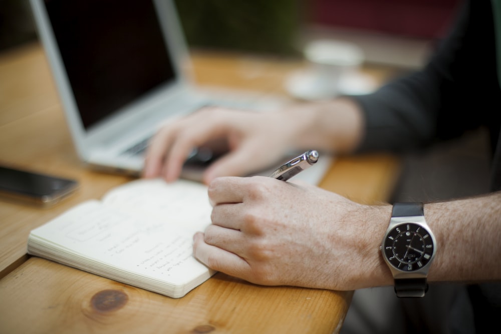 man sitting while writing on notebook