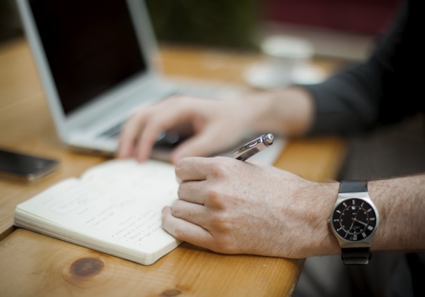 man sitting while writing on notebook