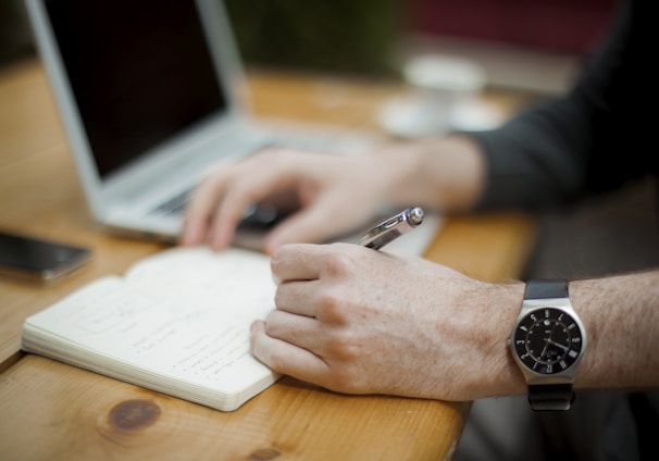 man sitting while writing on notebook