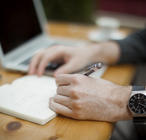man sitting while writing on notebook