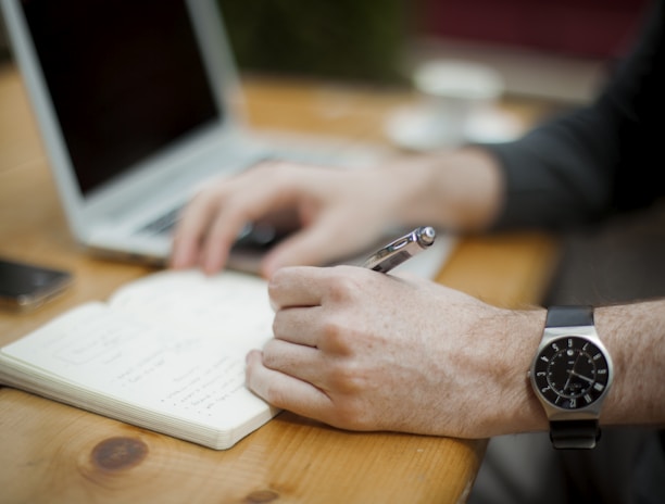 man sitting while writing on notebook