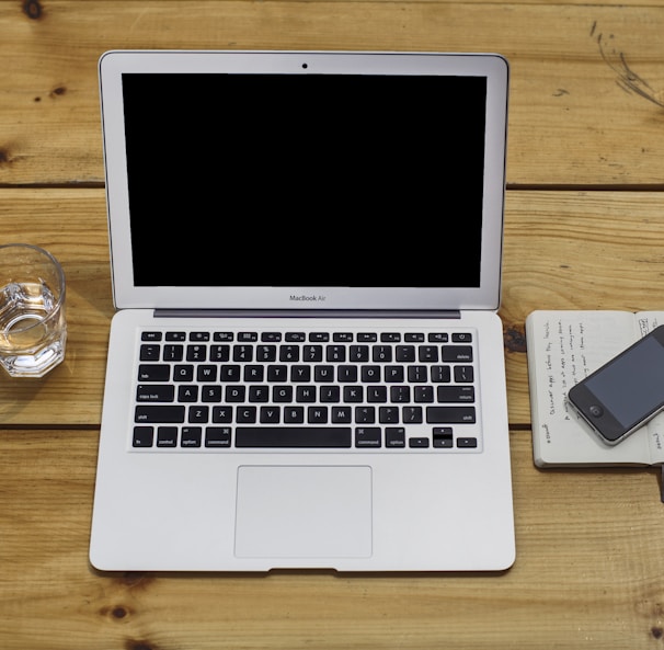 MacBook Air beside black iPhone 4 and drinking glass