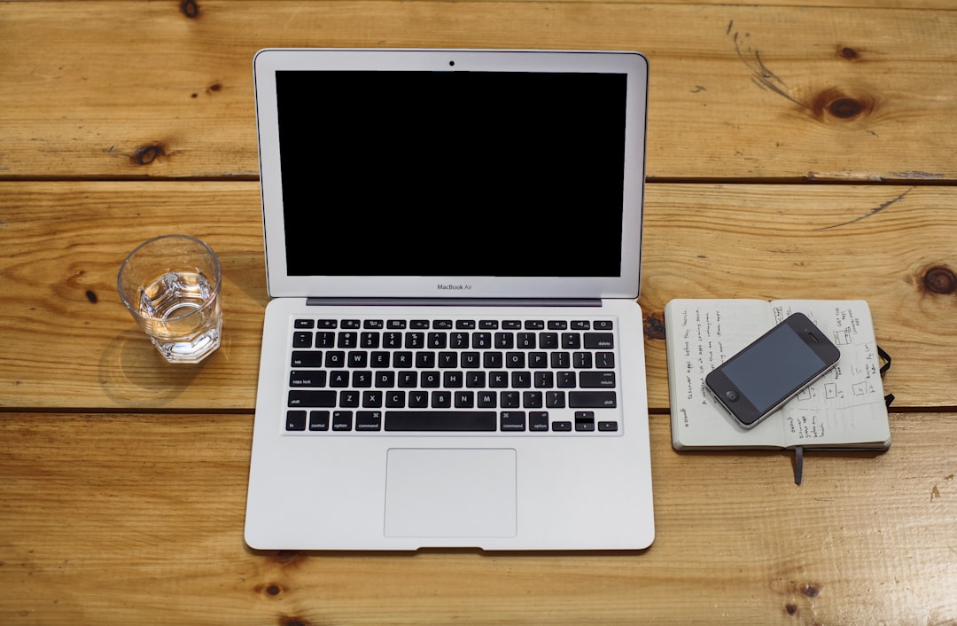An iPhone, a MacBook and a glass of water on a wooden surface