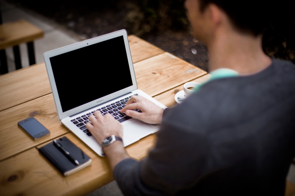 An over-the-shoulder shot of a man working on a MacBook outdoors