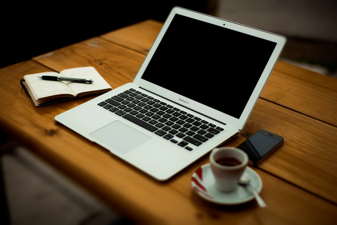Iphone, laptop, and pen on a table by Uniphonic MacBook Air on brown wooden table