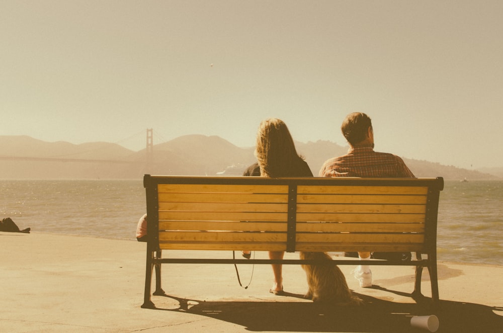 man and woman sitting on bench beside body of water