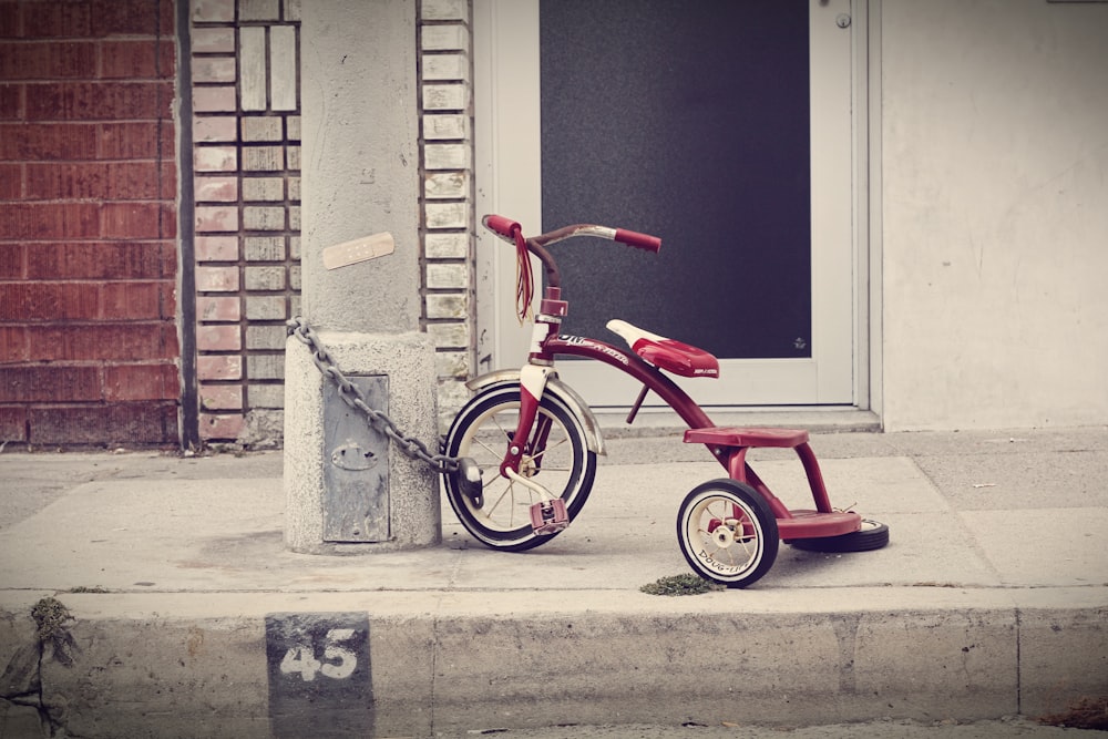 red and white Radio Flyer trike chained on stone post