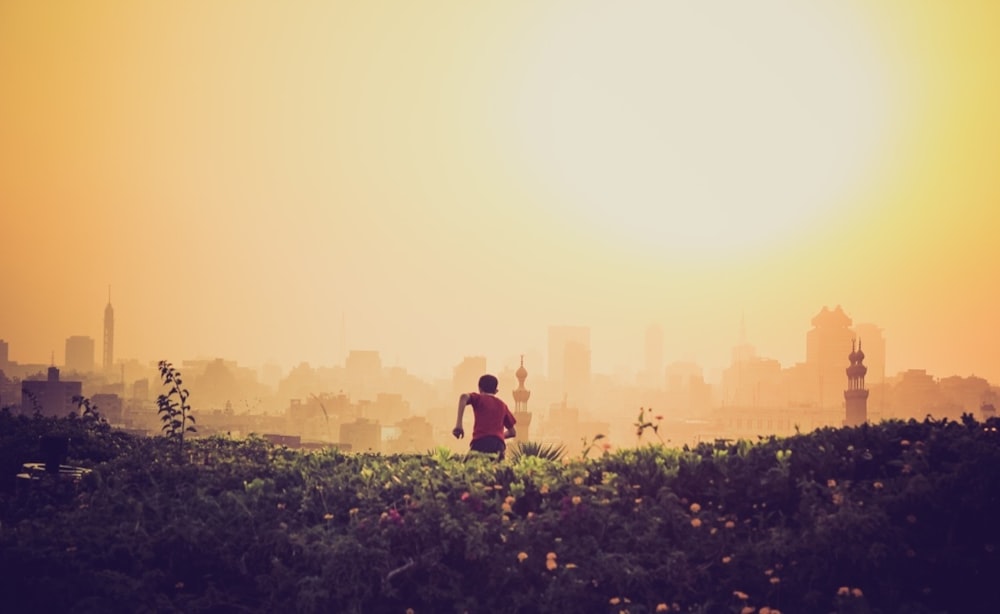 homme courant vers la ville sur le champ d’herbe verte pendant le temps d’or