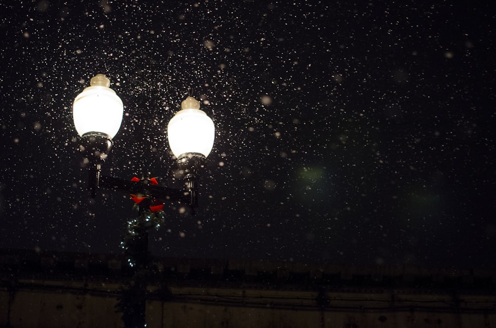 Photo en contre-plongée d’une lampe à 2 ampoules avec de la neige tombant pendant la nuit