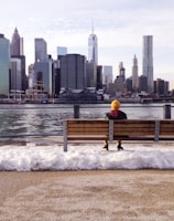 person in knit cap sitting on wooden bench in front of body of water during daytime