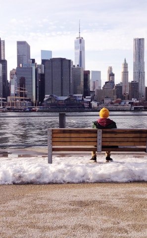 person in knit cap sitting on wooden bench in front of body of water during daytime