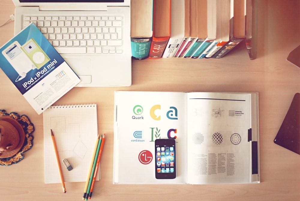 The top view of creative designer’s office showing books, pencils, laptop, and iphone on a desk