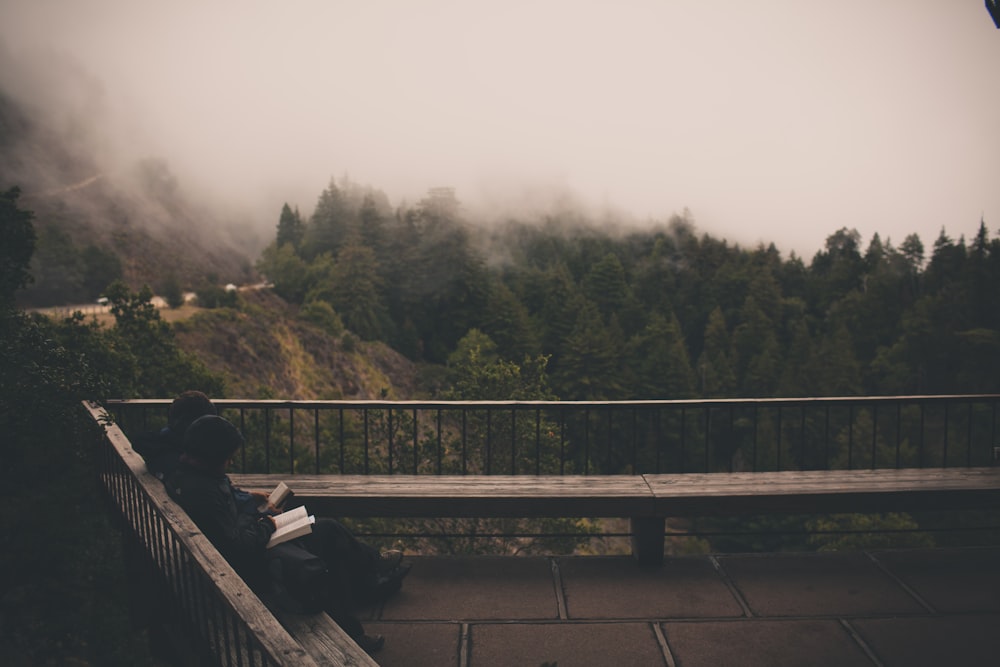 two people sitting on outdoor bench with cloudy sky and pine trees