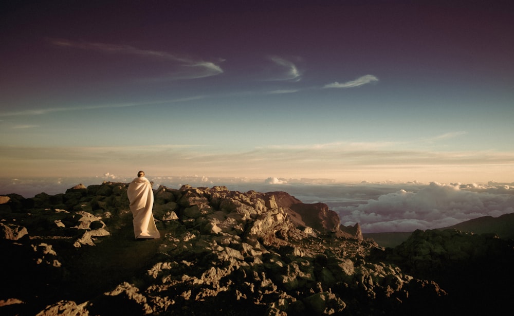 person wearing white robe on top of rocky mountain