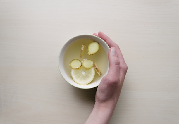 person holding white bowl with sliced lime and ginger inside