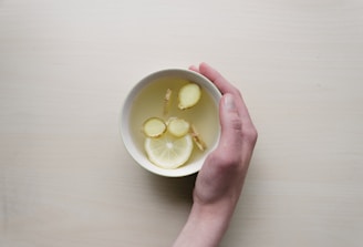 person holding white bowl with sliced lime and ginger inside