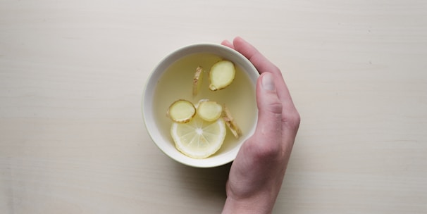 person holding white bowl with sliced lime and ginger inside