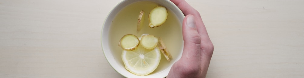 person holding white bowl with sliced lime and ginger inside