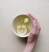 person holding white bowl with sliced lime and ginger inside