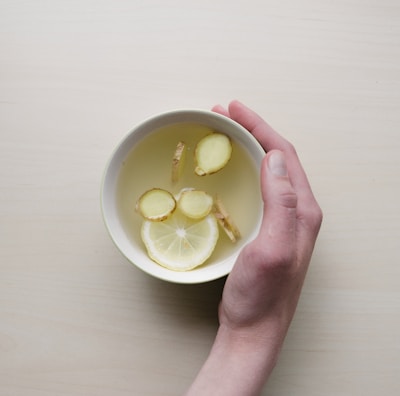 person holding white bowl with sliced lime and ginger inside