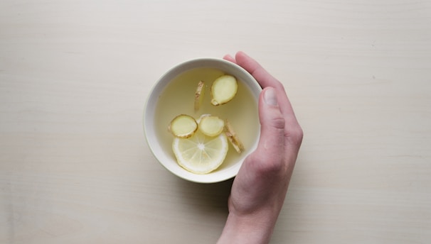 person holding white bowl with sliced lime and ginger inside