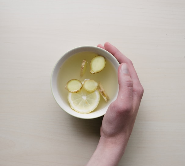 person holding white bowl with sliced lime and ginger inside