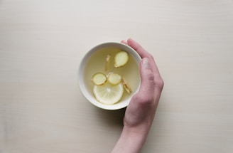 person holding white bowl with sliced lime and ginger inside