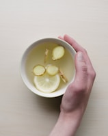 person holding white bowl with sliced lime and ginger inside