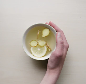 person holding white bowl with sliced lime and ginger inside