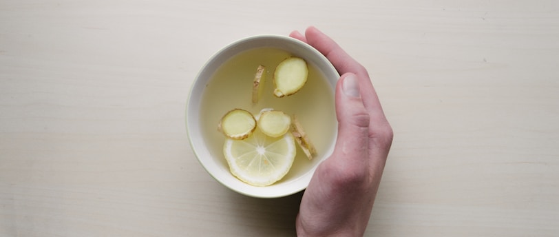 person holding white bowl with sliced lime and ginger inside