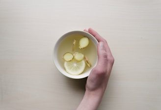 person holding white bowl with sliced lime and ginger inside