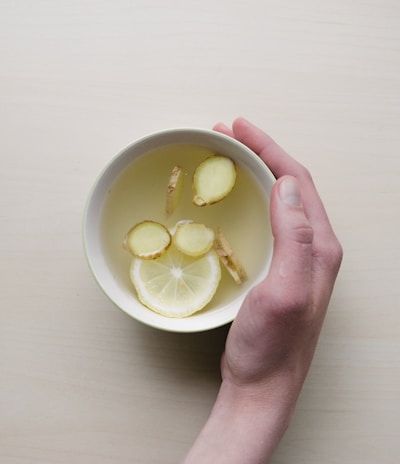 person holding white bowl with sliced lime and ginger inside