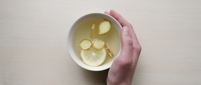 person holding white bowl with sliced lime and ginger inside