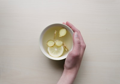 person holding white bowl with sliced lime and ginger inside