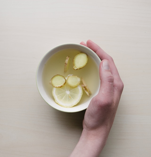 person holding white bowl with sliced lime and ginger inside