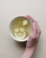 person holding white bowl with sliced lime and ginger inside