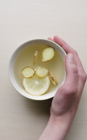 person holding white bowl with sliced lime and ginger inside
