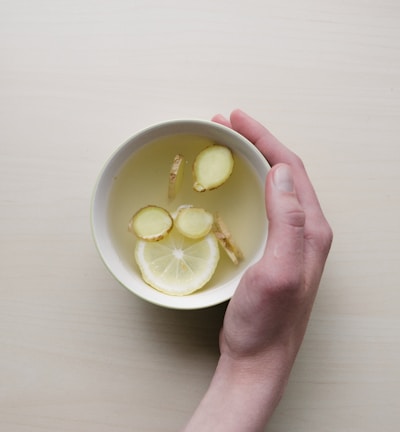 person holding white bowl with sliced lime and ginger inside